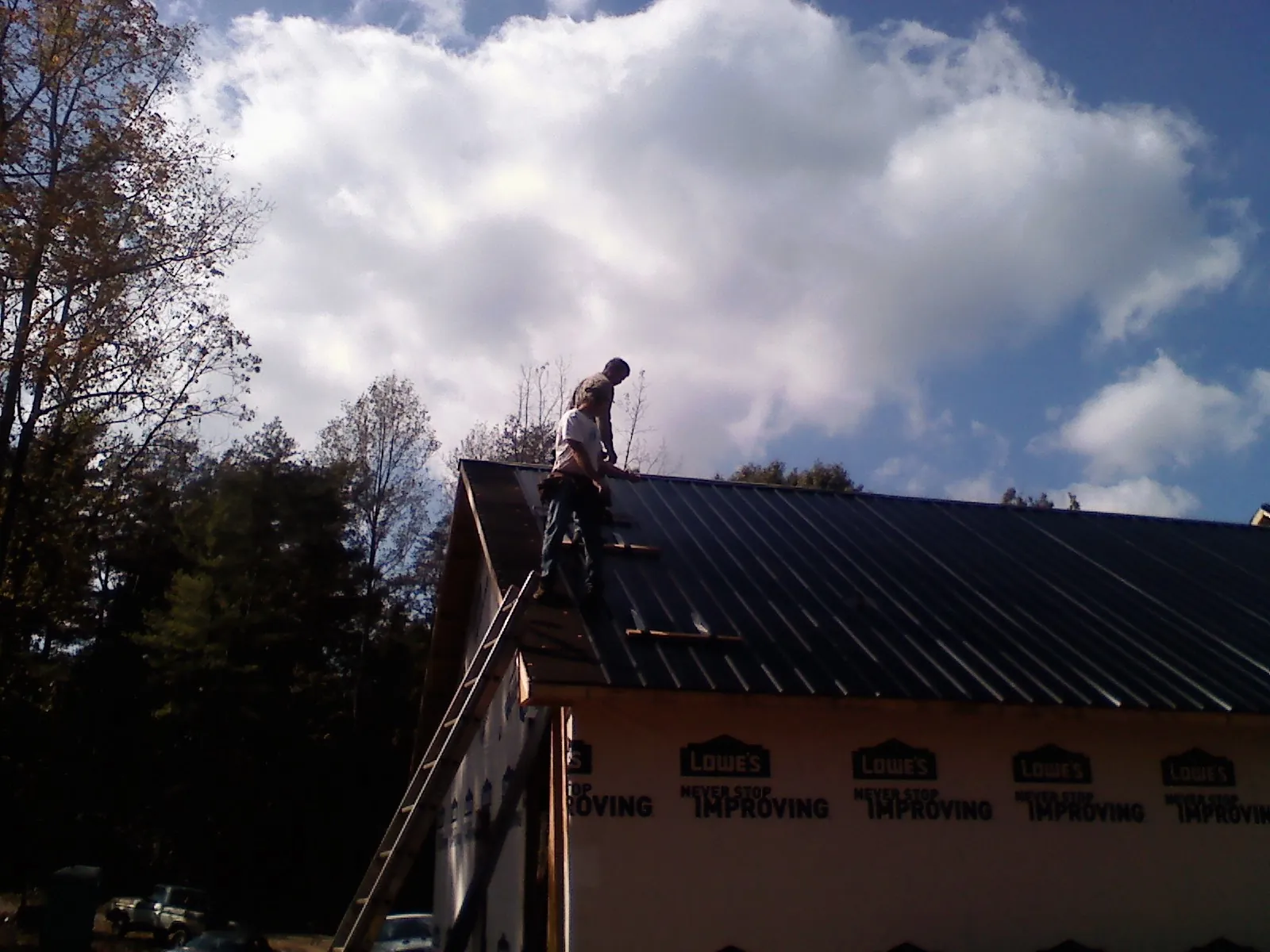 Roofer fastening dark metal panels high against a cloudy sky, from a Roof Inspection job in Churchville
