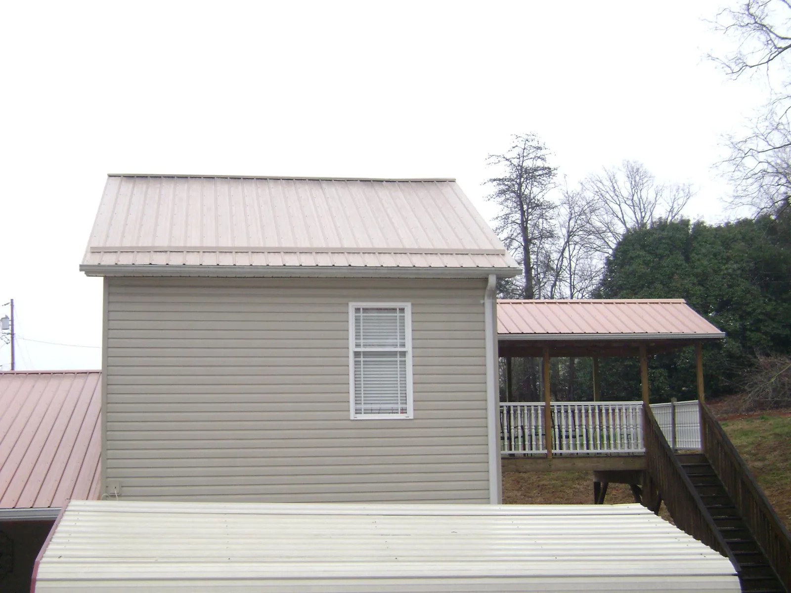 Tan metal roofs on a two story addition and attached porch, from a Roof Replacement job in Churchville